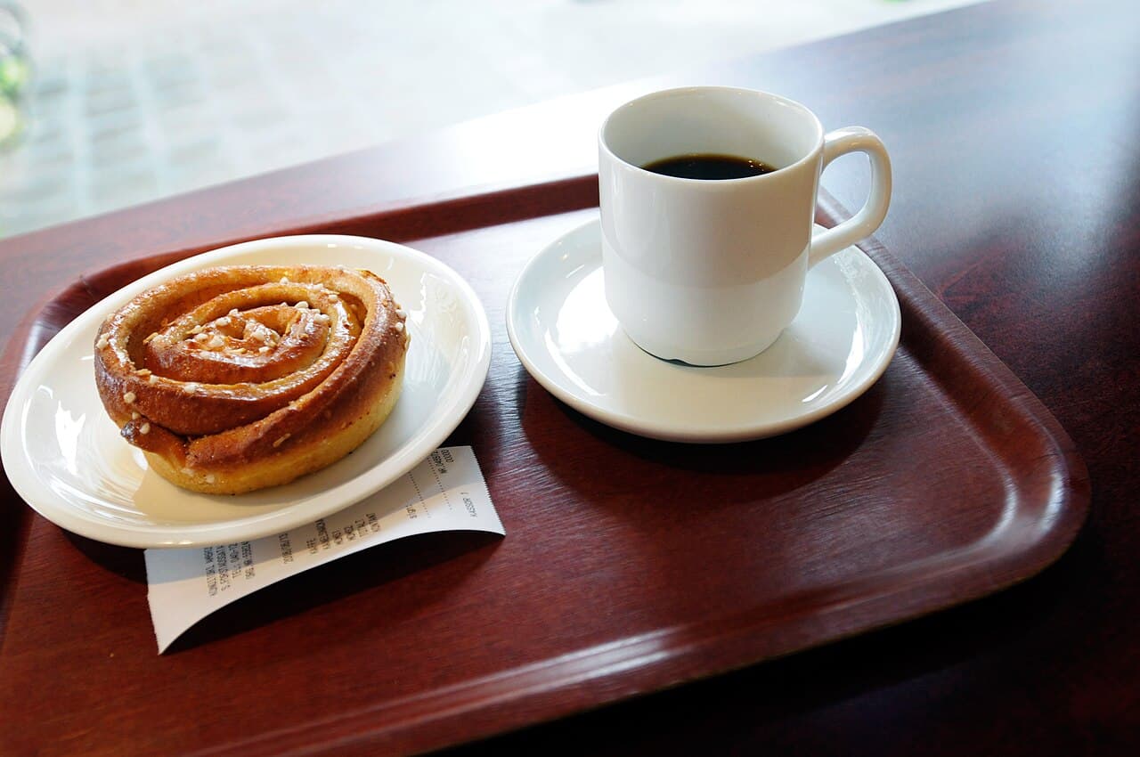 Fika: a cup of black kaffe and a kanelbulle on a wooden tray, rendered in ink and gold duotone.